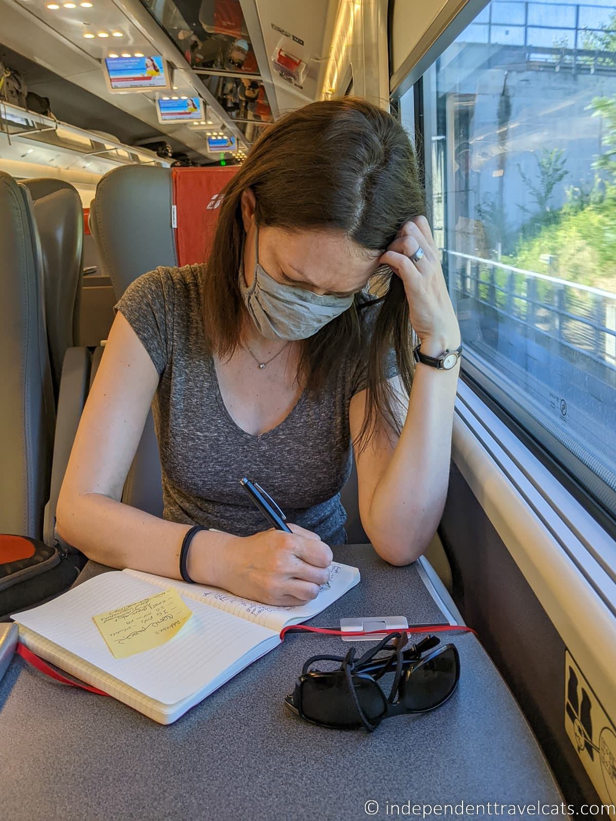 woman writing in journal on train best travel journal for travelers